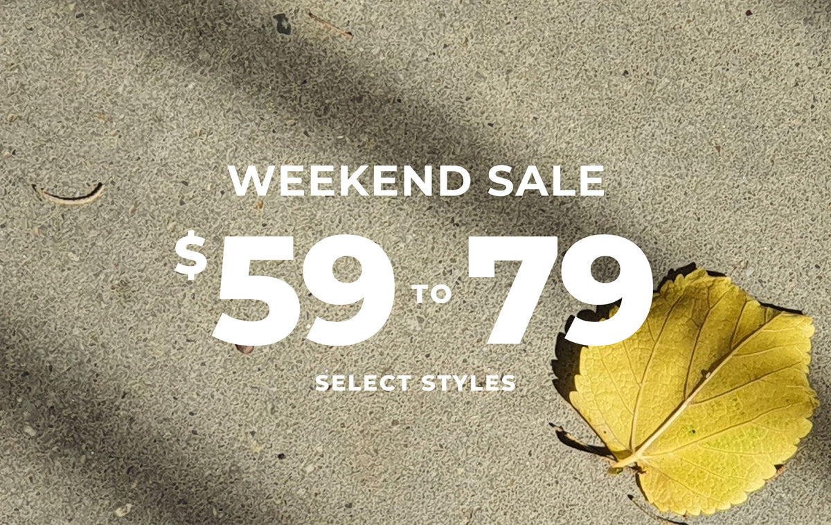 A promotional graphic with large white text reading 'WEEKEND SALE $59 TO 79' and 'SELECT STYLES' over a textured gray surface, with a yellow leaf placed on the right side.