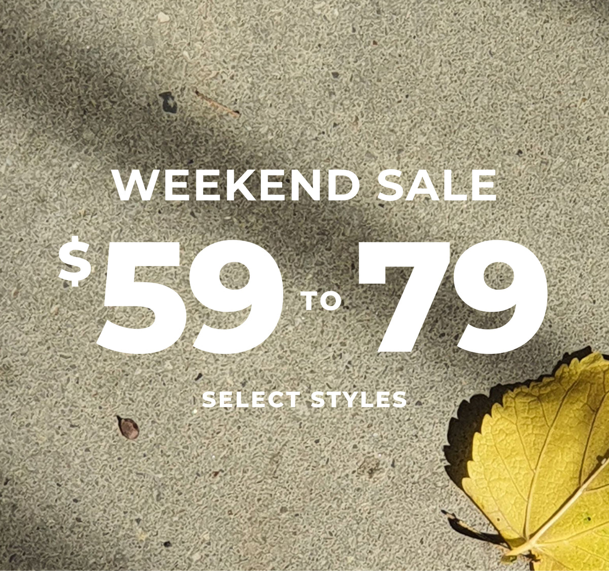A promotional sale graphic with large white text reading 'WEEKEND SALE $59 TO 79' and smaller text 'SELECT STYLES' over a textured gray pavement background, with part of a yellow leaf in the lower right corner.